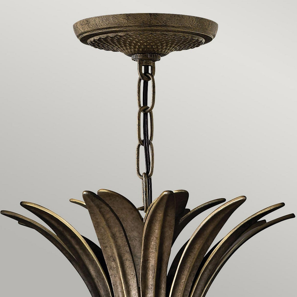 A Plantation 4 Light Pendant - Bronze chandelier, with a vintage-style that harks back to classic elegance, hangs gracefully from the ceiling on a chain. Its design, reminiscent of layered metal leaves or petals, adds an artistic flair against the plain light gray background.