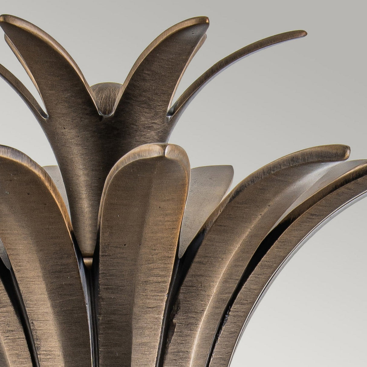 Close-up of the Plantation Outdoor 1 Light Medium Wall Lantern, showcasing its abstract, plant-like design with elongated, overlapping leaves in a burnished bronze finish. The lantern stands out against a light gray background.