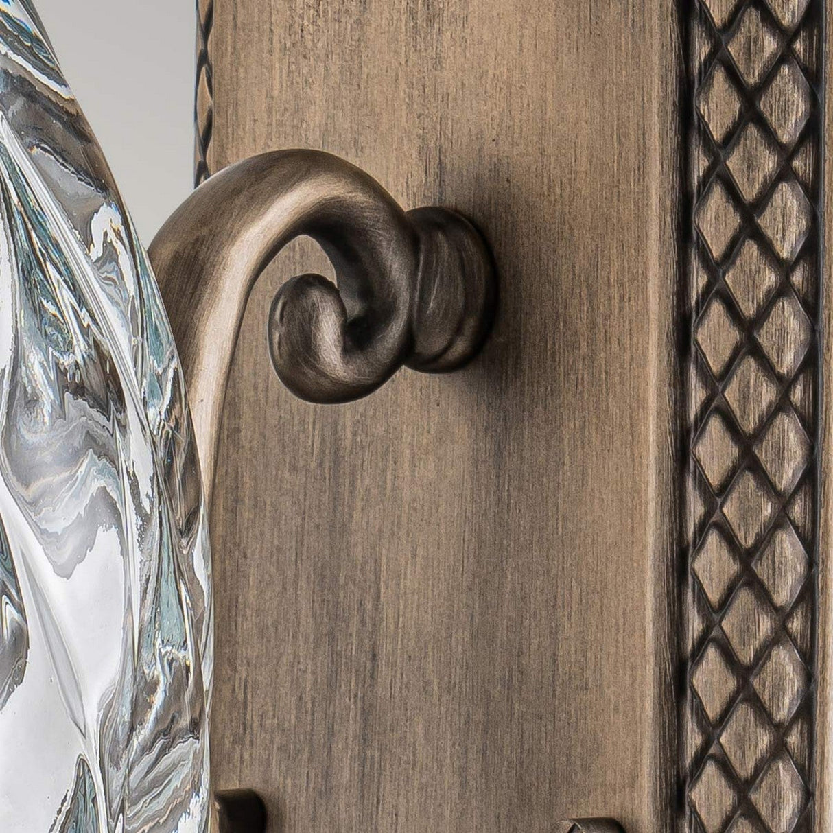 Close-up of the Plantation Outdoor 1 Light Medium Wall Lantern in a burnished bronze finish. It showcases an intricate, curved design with a striking pineapple optic glass component. The background reveals a diamond pattern on the metal, emphasizing its craftsmanship.