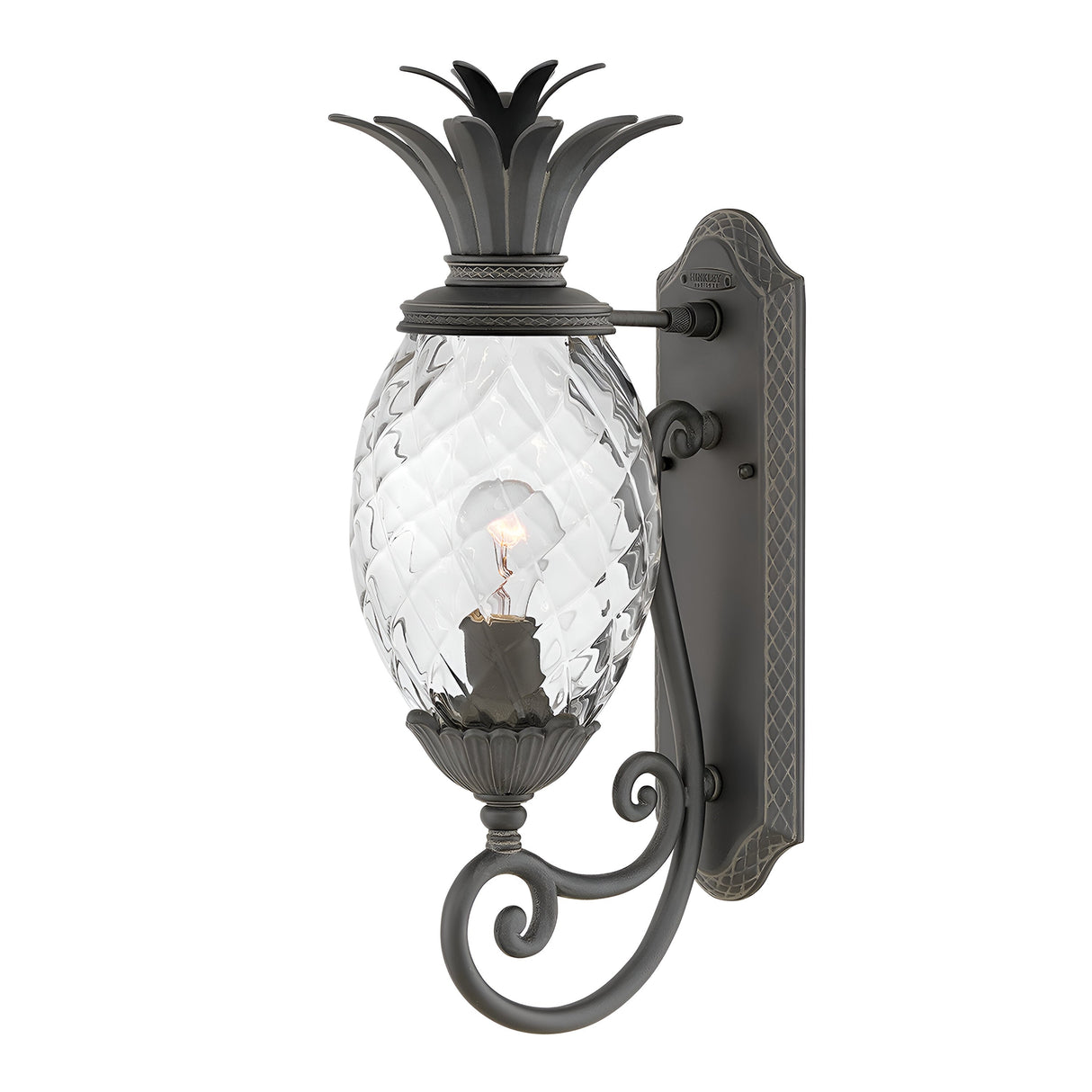 Introducing the Plantation Outdoor 1 Light Medium Wall Lantern in Black, featuring a pineapple-shaped glass design and an ornate metal frame. The light bulb inside casts a gentle glow, highlighting the intricate scrollwork of this sophisticated black wall lantern.