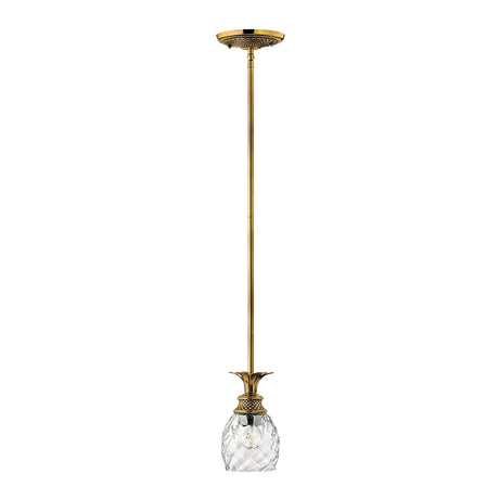 The Plantation 1 Light Pendant in Burnished Brass features a vintage design with decorative elements and is elegantly suspended from the ceiling by a slender brass rod. The fixture showcases an intricately carved, clear optic glass shade adorned with a floral motif.