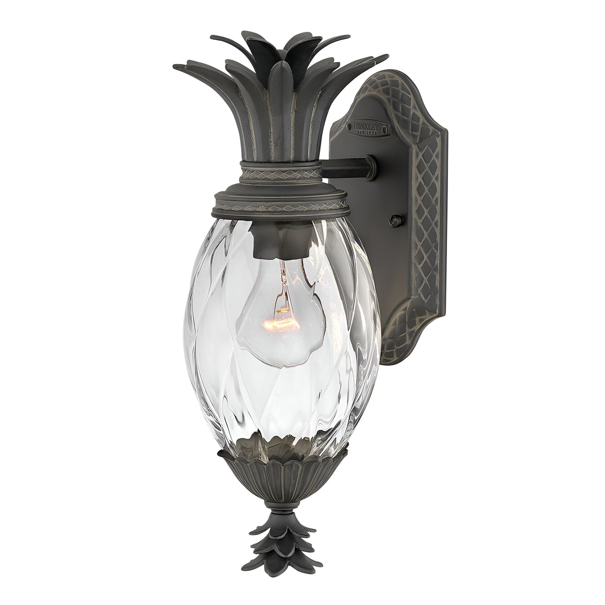 Introducing the Plantation Outdoor 1 Light Small Wall Lantern - Black, featuring a charming pineapple-shaped glass body with a clear, textured finish and dark metal accents. Its stylish black finish enhances its allure, allowing the visible bulb inside to cast an inviting glow. The backplate is adorned with a decorative pattern for added elegance.