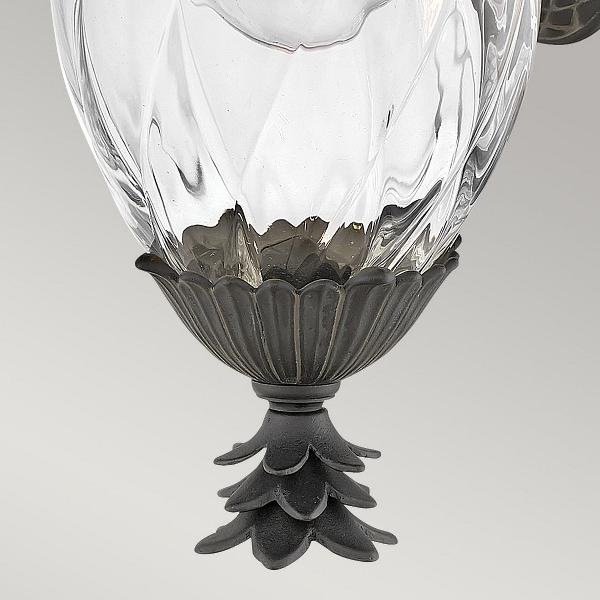 Close-up view of the Plantation Outdoor 1 Light Small Wall Lantern in black, featuring an ornate, clear glass body with a decorative floral base and a layered, textured design reminiscent of pineapple optic glass. The background is light gray.
