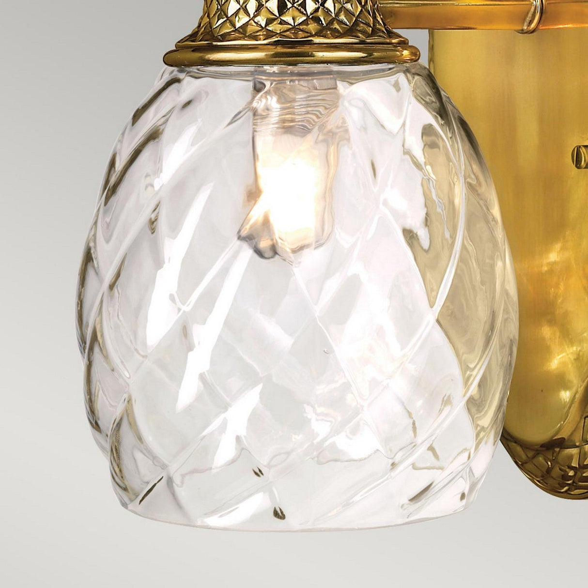 Close-up of the Plantation Outdoor 1 Light Wall Light - Burnished Brass, showcasing its pineapple-shaped optic glass shade with a diamond pattern. The fixture emits a warm glow from its lit bulb and features elegant burnished brass elements.