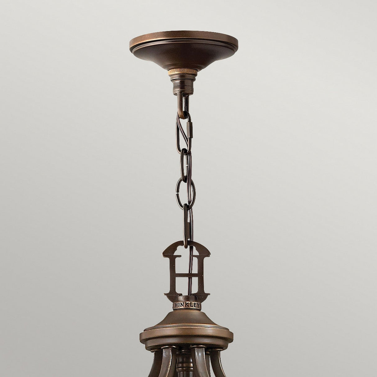 Close-up view of the Plymouth 15 Light Chandelier in a vintage-inspired bronze finish, featuring a chain link attachment to the ceiling. The focus is on the ceiling mount and the beginning of the fixture, set against a plain background.