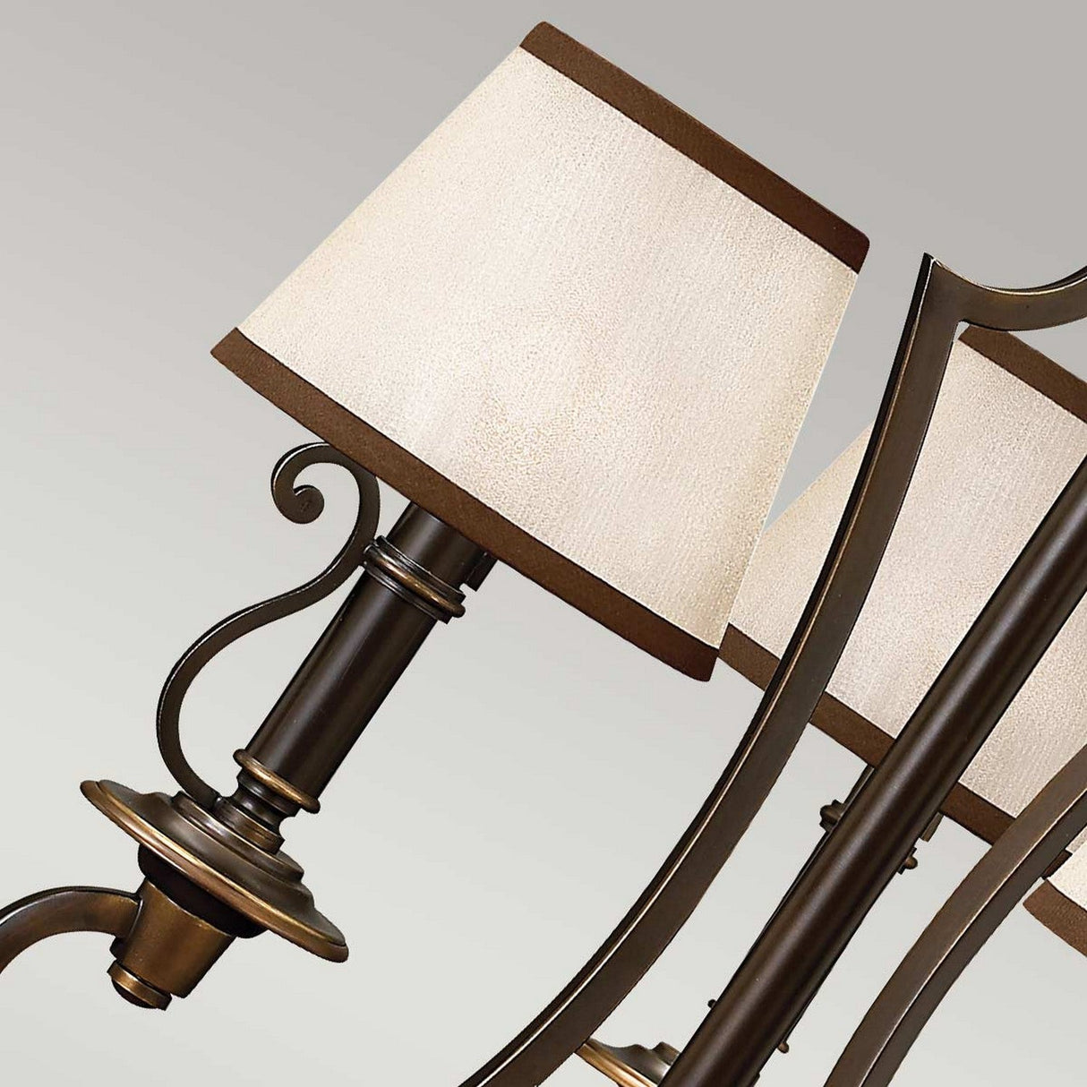 Capture the elegance of a bronze wall sconce that showcases a cream fabric lampshade with brown trim. This vintage-inspired lighting piece features detailed scrollwork on the arm, adding sophistication against a neutral backdrop, echoing the allure of the Plymouth 3 Light Chandelier - Bronze.