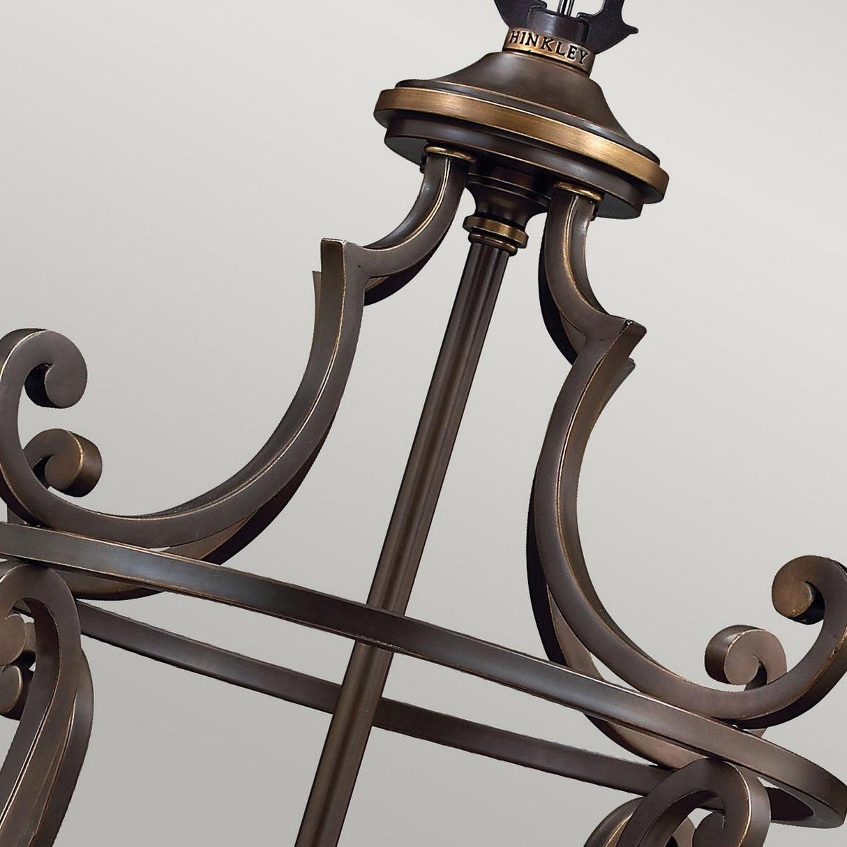 A close-up of a decorative bronze chandelier frame in an Old Bronze shade showcases elegant scrollwork and intricate detailing. The Hinkley brand name is prominently displayed on top, reflecting a vintage-inspired design reminiscent of the Plymouth 4 Light Chandelier - Bronze.