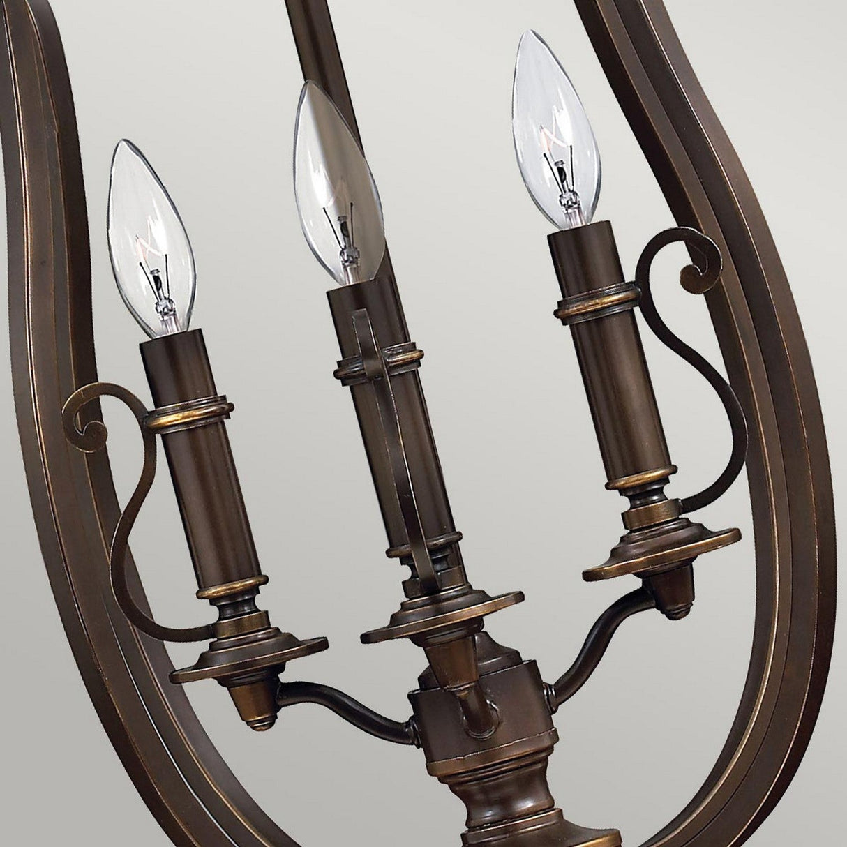 Close-up of the stylish Plymouth 4 Light Chandelier in its elegant bronze finish, featuring four candle-shaped light bulbs that highlight its intricate scroll details and gracefully curving frame. The old bronze hue accentuates its vintage-inspired design, while clear candle-like bulbs contribute to a classic ambiance in this enchanting décor piece.