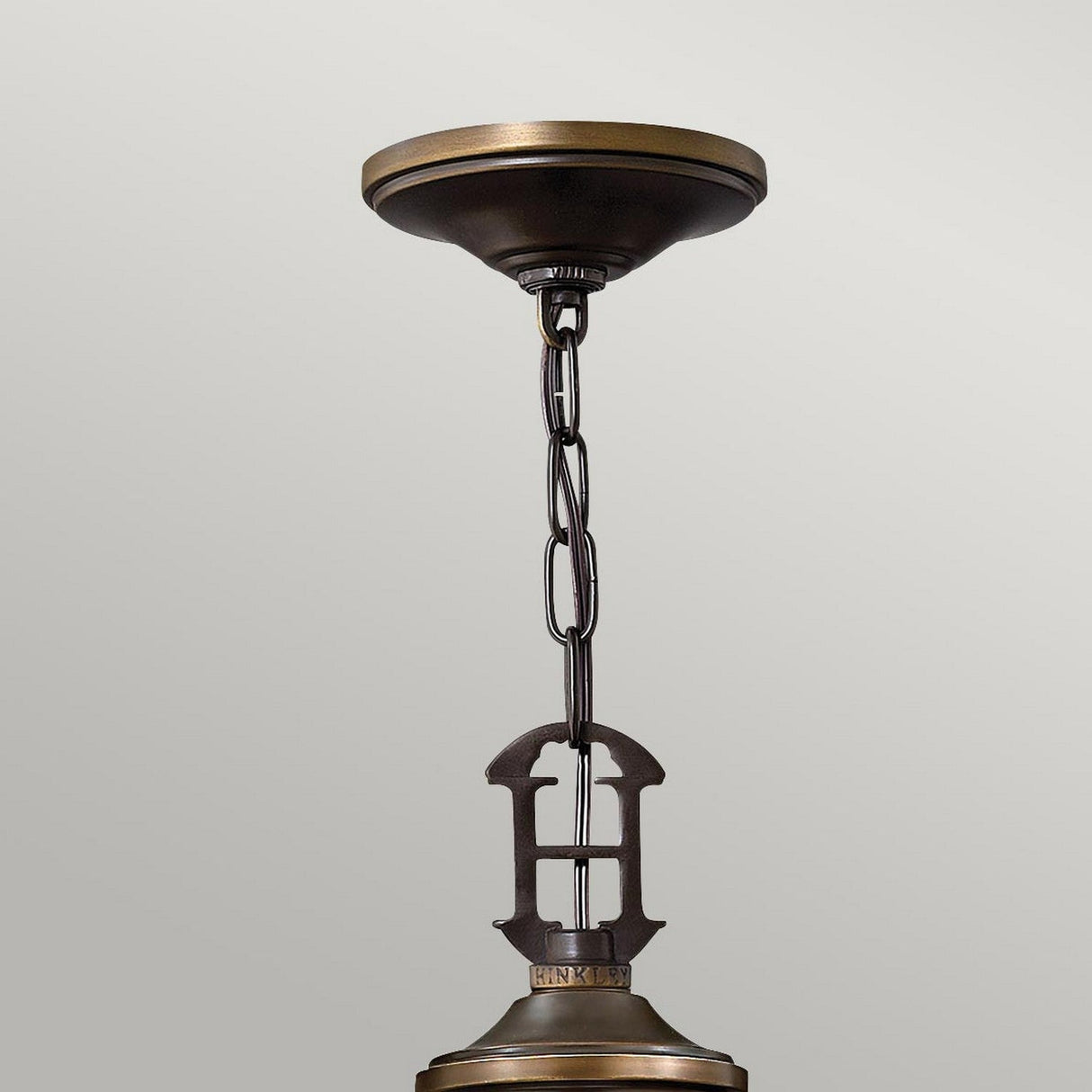 The Plymouth 9 Light Chandelier - Bronze showcases an Old Bronze finish complete with a chain and decorative hook, elegantly attached to a ceiling plate. Its vintage-inspired candle sleeves add to its charm, beautifully contrasted against a light gray background.