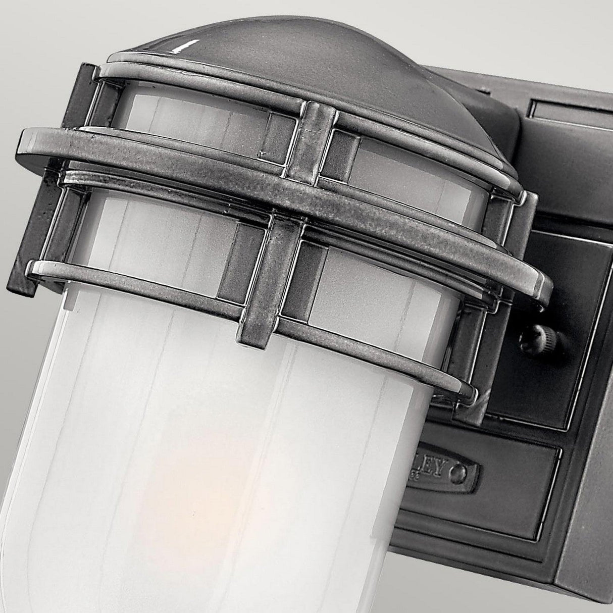 Close-up of the Reef Outdoor Mini 1 Light Lantern in grey, showcasing an industrial-style design with a cylindrical frosted glass shade encased in a metal cage. The durable cast aluminum frame features a rectangular base with a small switch, boasting a sleek black finish for added durability and an IP44 rating for weather resistance.