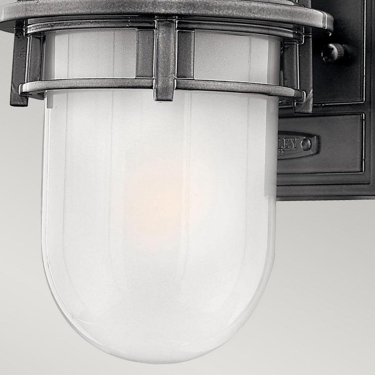 Introducing the Reef Outdoor Mini 1 Light Lantern in Grey: This vintage-style wall sconce light fixture features a frosted glass dome and metal accents, mounted on a rectangular backplate. Its cast aluminium frame ensures durability, and with an IP44 rating, it's ideal for outdoor use while emitting a soft, warm glow.