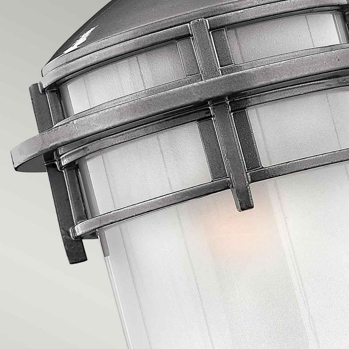 Close-up of a modern industrial-style outdoor light fixture crafted from cast aluminium with a gray metal frame and frosted glass. The design, inspired by the Reef Outdoor Small 1 Light Lantern - Grey, features geometric metal bars and boasts an IP44 rating for durability.