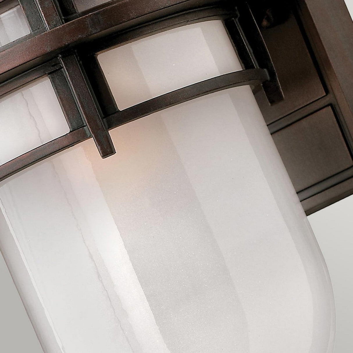 Close-up of the Reef Outdoor Small 1 Light Lantern - Bronze, featuring a frosted white cylindrical glass within a bronze metal frame. With its IP44 rating and horizontal and vertical bands, this lantern's modern design is ideal for various outdoor applications against a plain background.