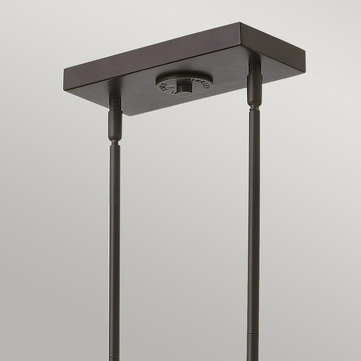 This detailed image features the Rigby 3 Light Island Chandelier - Bronze & Brass, drawing attention to its dark rectangular ceiling mount. It has a bronze and brass finish with two metal rods descending at even intervals from beneath, reflecting an industrial and vintage aesthetic against a neutral backdrop.