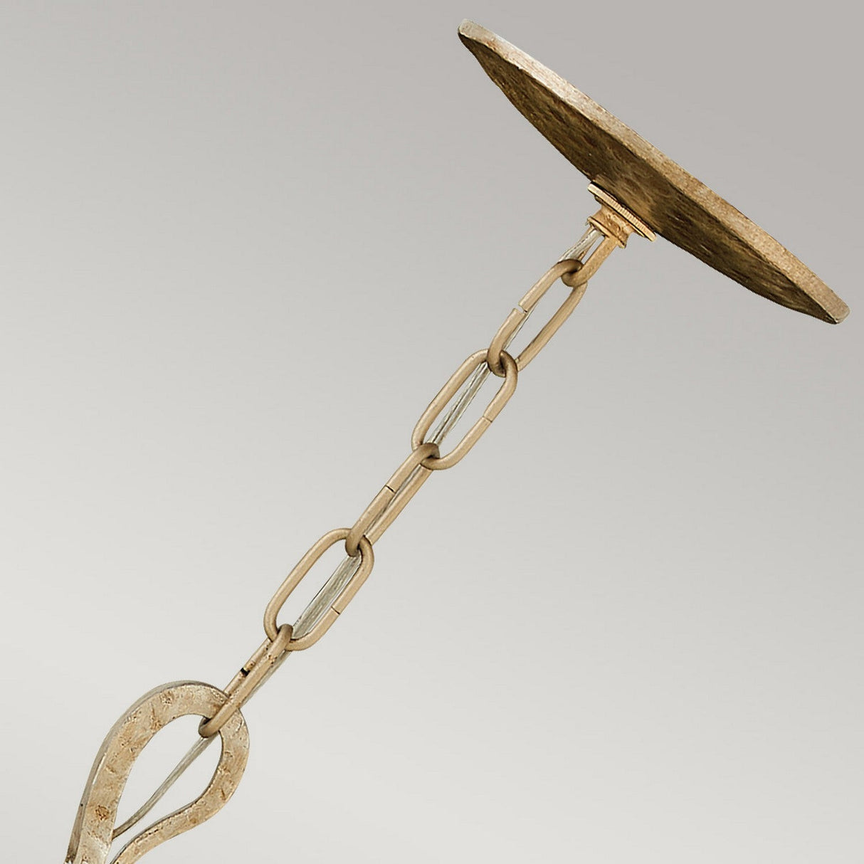 Close-up of the Spyre 6 Light Chandelier in Champagne Gold, featuring a metal hanging chain with a round ceiling plate. The large connected chain links ascend to the circular plate, all showcasing a rustic metallic finish. This chandelier captures elegance in its design while maintaining a neutral backdrop.