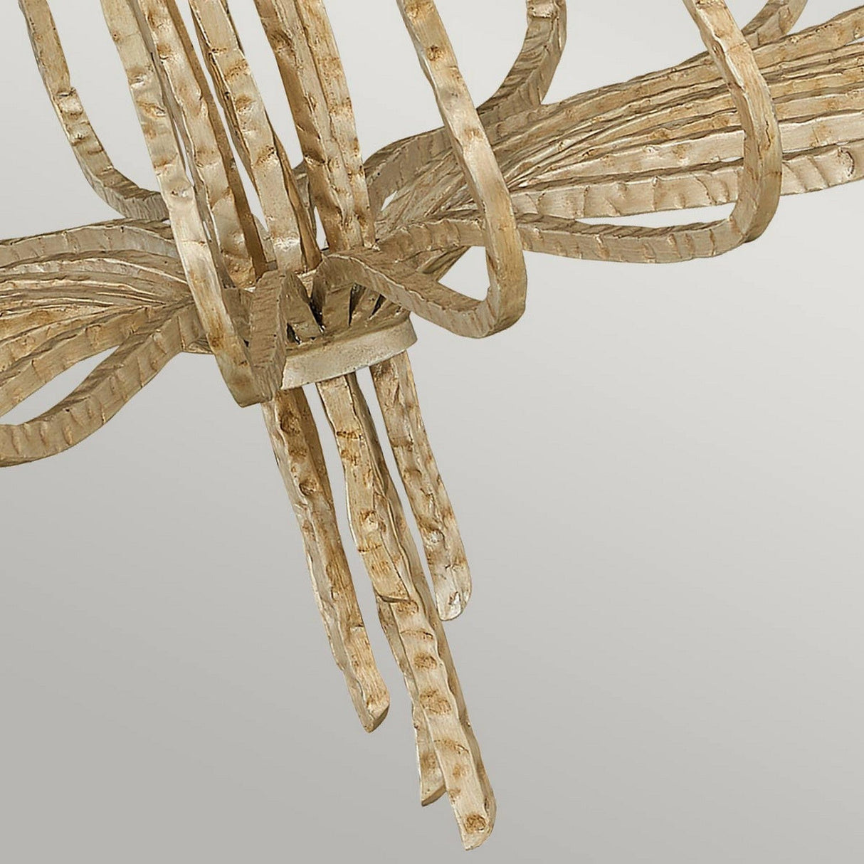 A close-up of an intricate metal sculpture features twisted, ribbon-like details in a Champagne Gold finish, reminiscent of the elegant design of the Spyre 6 Light Chandelier. Set against a light gray background, the sculpture's texture and curves form a dynamic and abstract masterpiece.