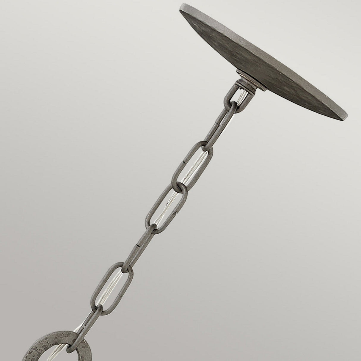 Close-up of the Spyre 6 Light Chandelier in Metallic Matte Bronze, showcasing its industrial-edge metal chain with oval links. The chain connects to a flat, round disc at the top and a larger circular ring at the bottom against a plain background.