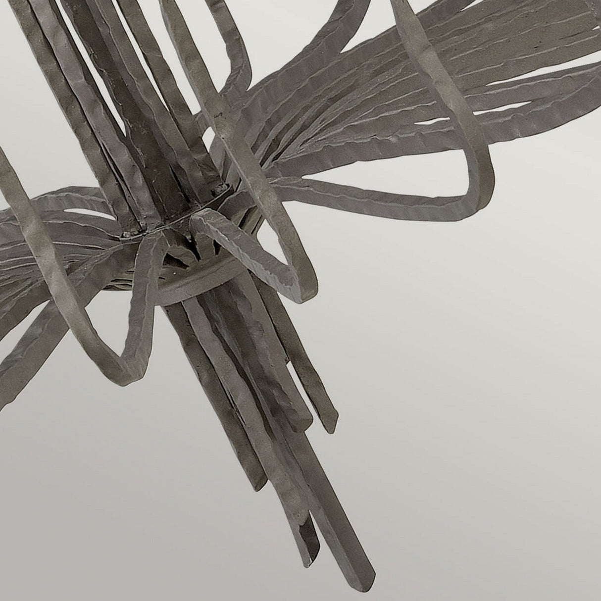 A close-up of the Spyre 6 Light Chandelier in metallic matte bronze, featuring gracefully intertwined elongated strips, set against a smooth, light gray background.