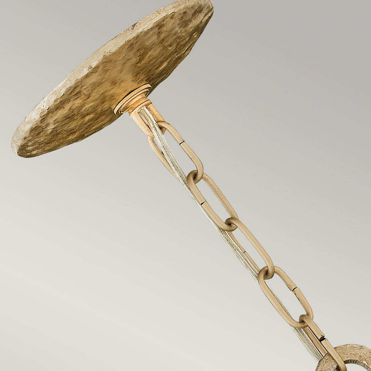 A close-up of the Spyre 6 Light Pendant in Champagne Gold highlights a distinctive ceiling fixture with a textured, stone-like base and chain-like stem, perfectly complementing versatile decor styles against a neutral background.