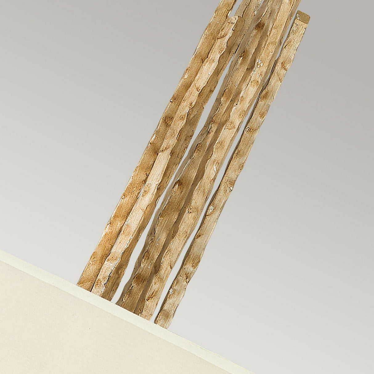 A close-up view features several textured, vertical elements emerging from a Champagne Gold box. These elements possess a rough, wavy surface and are light brown. The positioning of the box is in the bottom left corner against a simple, light-colored backdrop. This design pairs beautifully with various decor styles and is epitomized by the Spyre 6 Light Pendant in Champagne Gold.