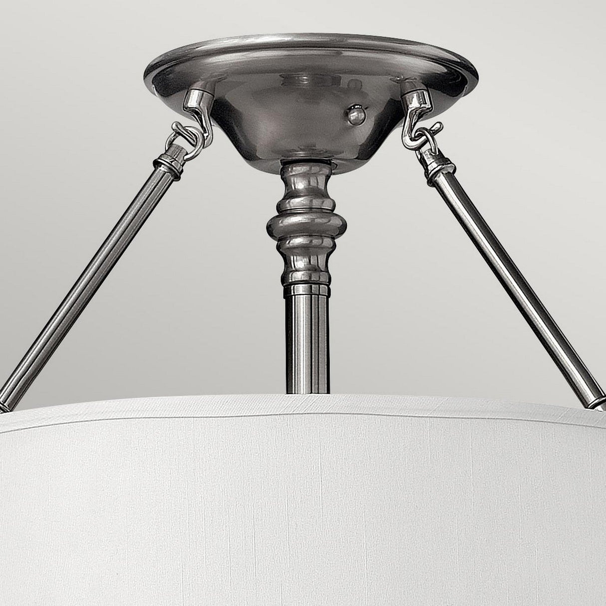 A close-up of the Sussex 3 Light Semi Flush in brushed nickel showcases its modern and sleek design, featuring a cylindrical white fabric shade. The fixture is supported by three angled rods connected to a circular base, all rendered in a sophisticated brushed metal finish.