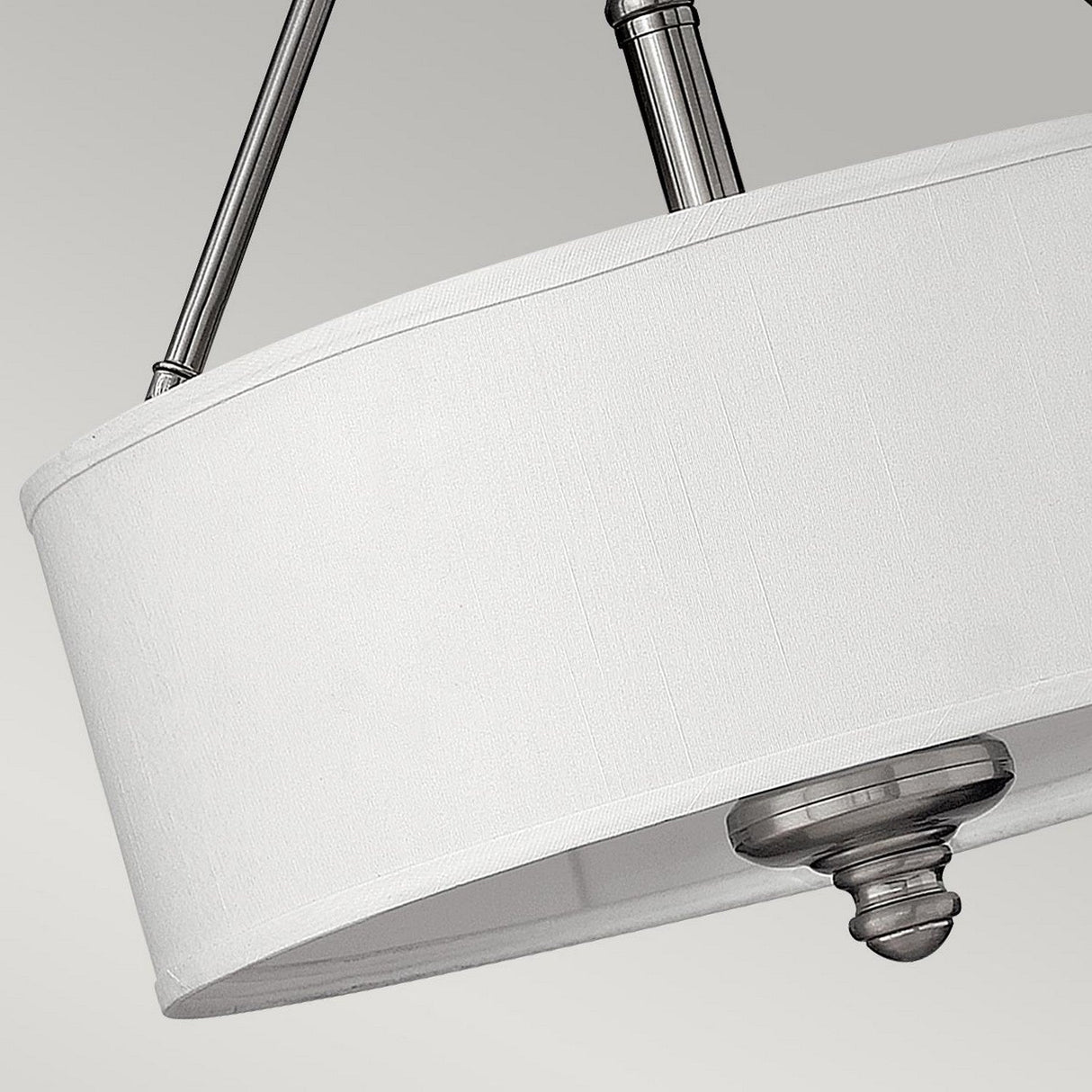 A close-up view of the Sussex 3 Light Semi Flush fixture showcases its modern aesthetic with a white drum-shaped fabric lampshade, complemented by elegant brushed nickel accents, all set against a neutral background.