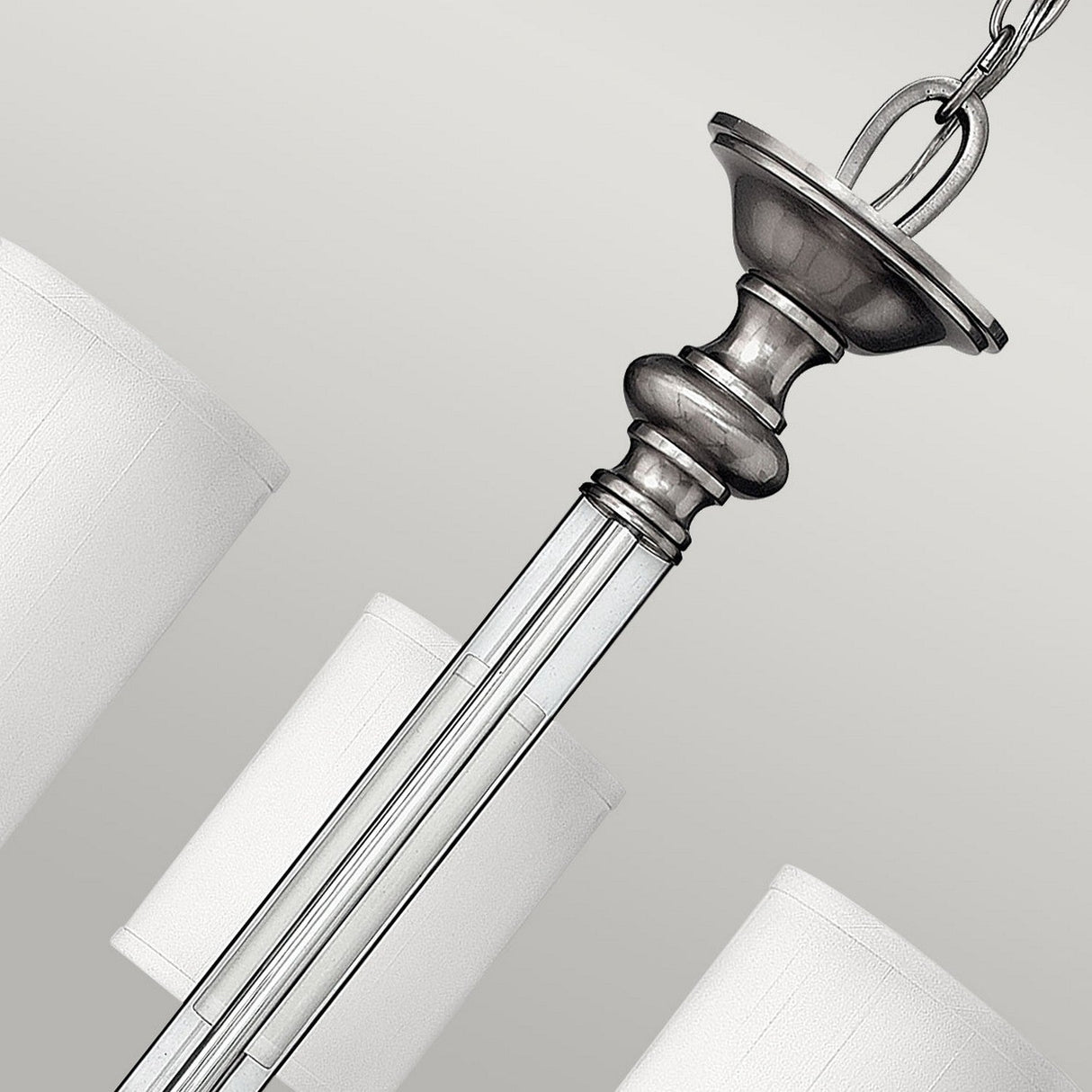 A close-up of the Sussex 5 Light Chandelier - Brushed Nickel reveals its elegant design, featuring cylindrical white lampshades and a polished metal central stem suspended by a chain. The brushed nickel finish imparts traditional charm, and the chandelier's sophisticated design is accentuated against a soft gray background.