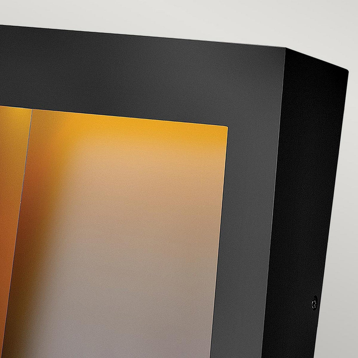Close-up view of a sleek, modern, Taper Outdoor LED Large Wall Lantern in black reflecting a warm, amber light. The lantern's frame features a minimalist design that resembles a contemporary mirror, creating an elegant look that complements outdoor lighting aesthetics.
