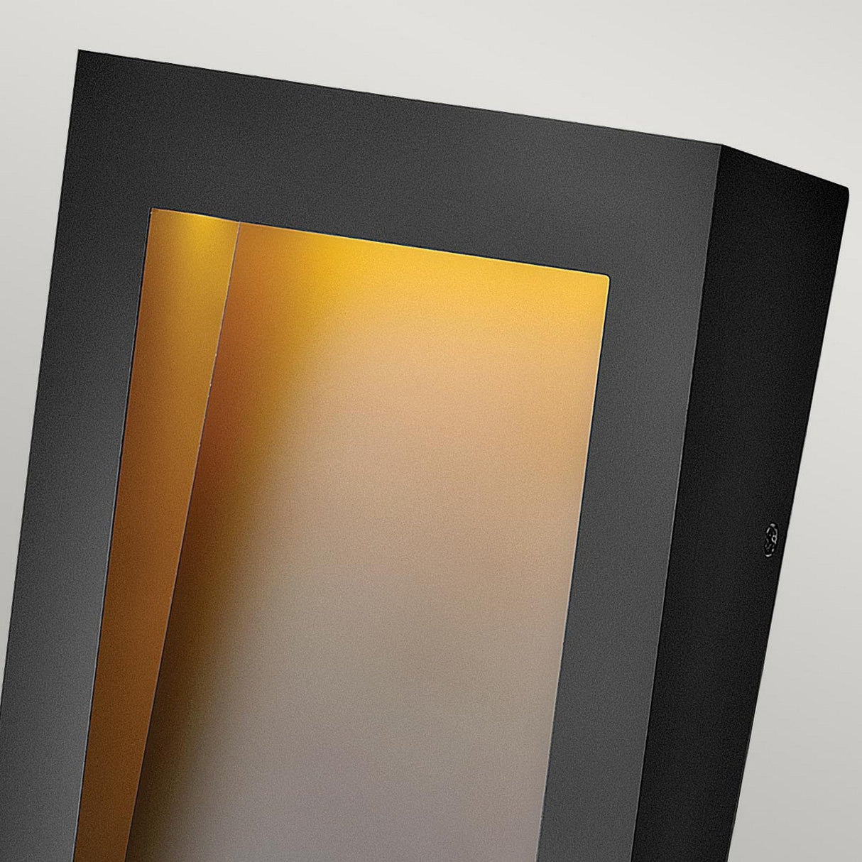 The Taper Outdoor LED Small Wall Lantern in black features a modern rectangular design with an angled opening, providing energy-efficient lighting that casts a warm yellowish glow against a light grey backdrop. This outdoor wall light serves as a chic and contemporary lighting solution for any space.