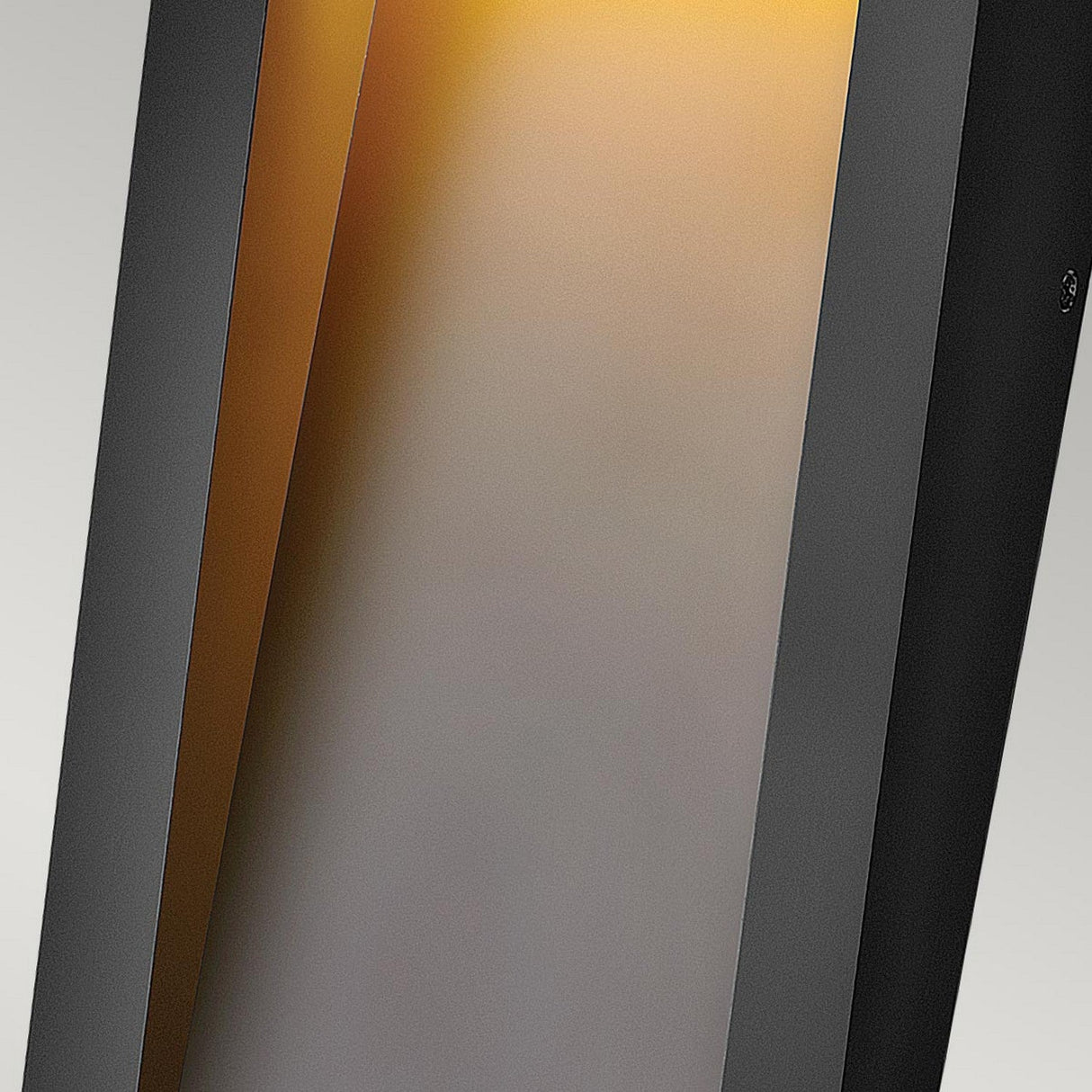 Close-up of the Taper Outdoor LED Small Wall Lantern - Black, a modern lighting solution that radiates a warm amber glow. The lantern's sleek black frame provides soft, energy-efficient illumination against a neutral background, making it an ideal enhancement for any space.