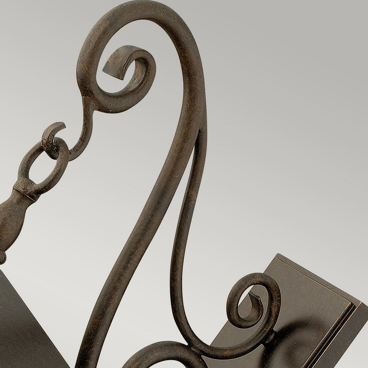 A close-up of the Trellis Outdoor 4 Light Large Wall Lantern in bronze reveals its ornate, dark metal scroll design with curved and intricate detailing set against a light gray background. This elegant wrought iron structure is reminiscent of an outdoor decorative fixture or piece of furniture.