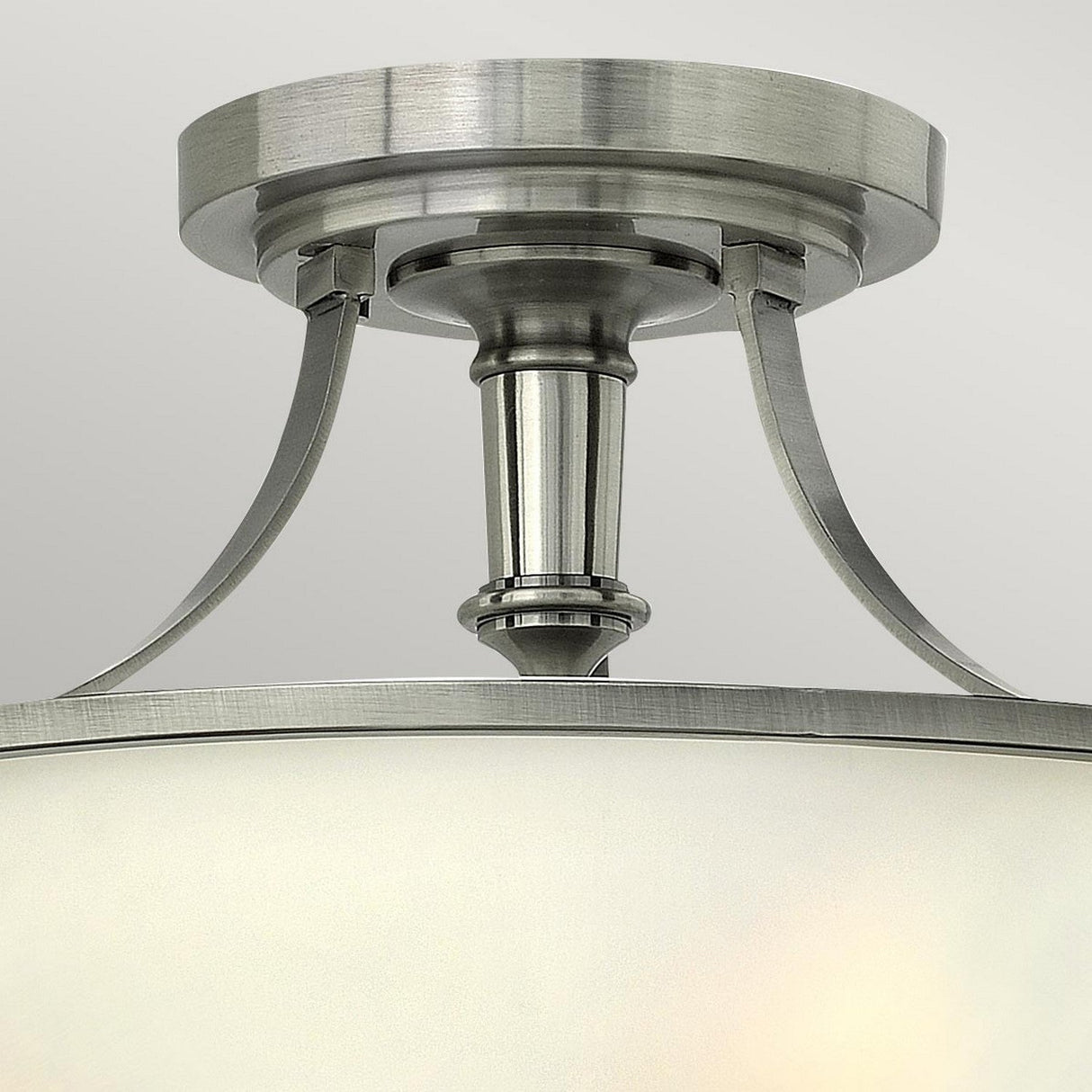 The Truman 3 Light Semi Flush in Antique Nickel features an elegant design with a cylindrical mount and curved supports. Its frosted glass shade, enhanced by etched opal glass accents, delivers a modern aesthetic against a neutral backdrop.