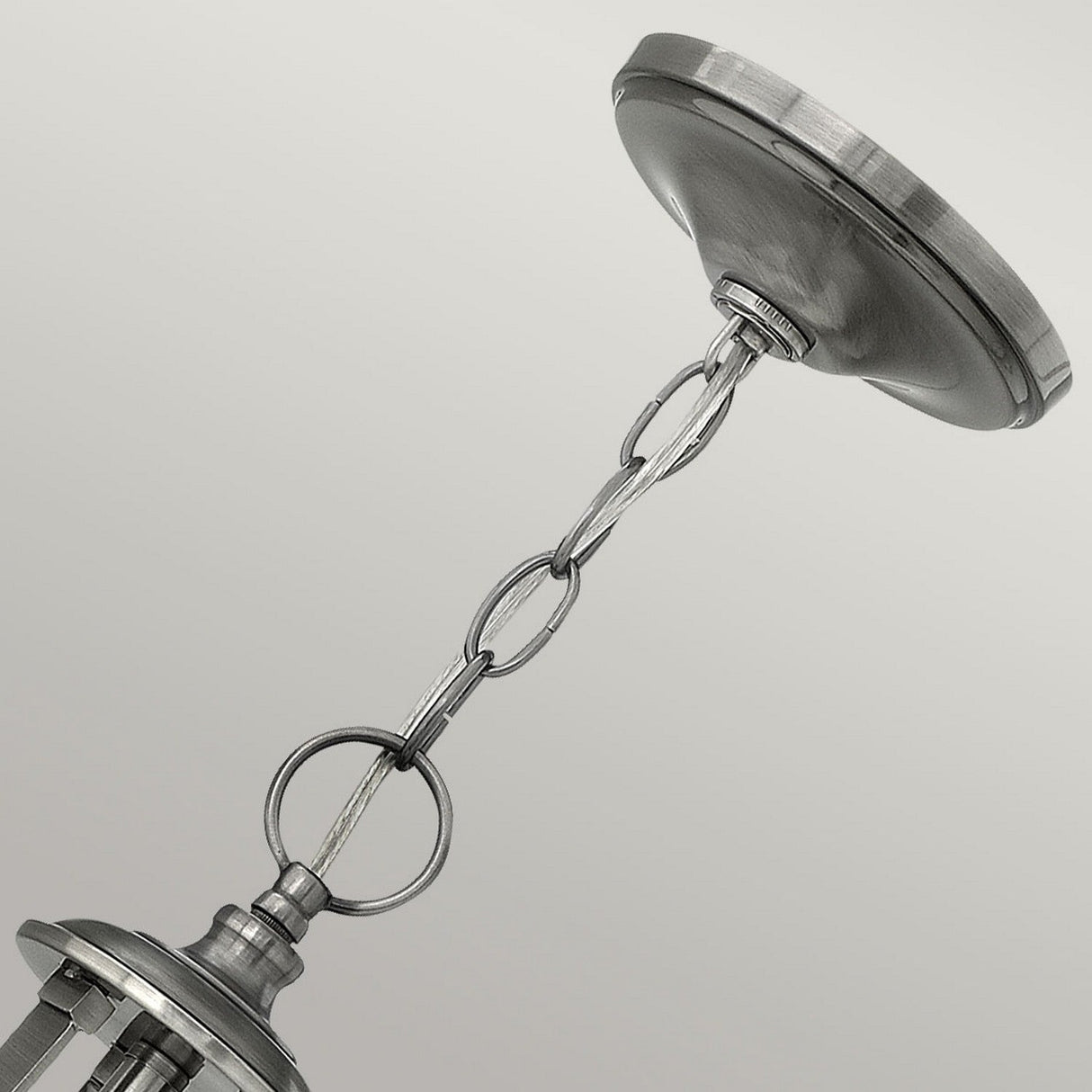 A close-up image showcases the metallic chain and canopy of the Truman 3 Light Chandelier - Antique Nickel, highlighting its interlinked loops and sleek silver finish. This elegant chandelier features an etched opal glass shade, beautifully set against a light backdrop.