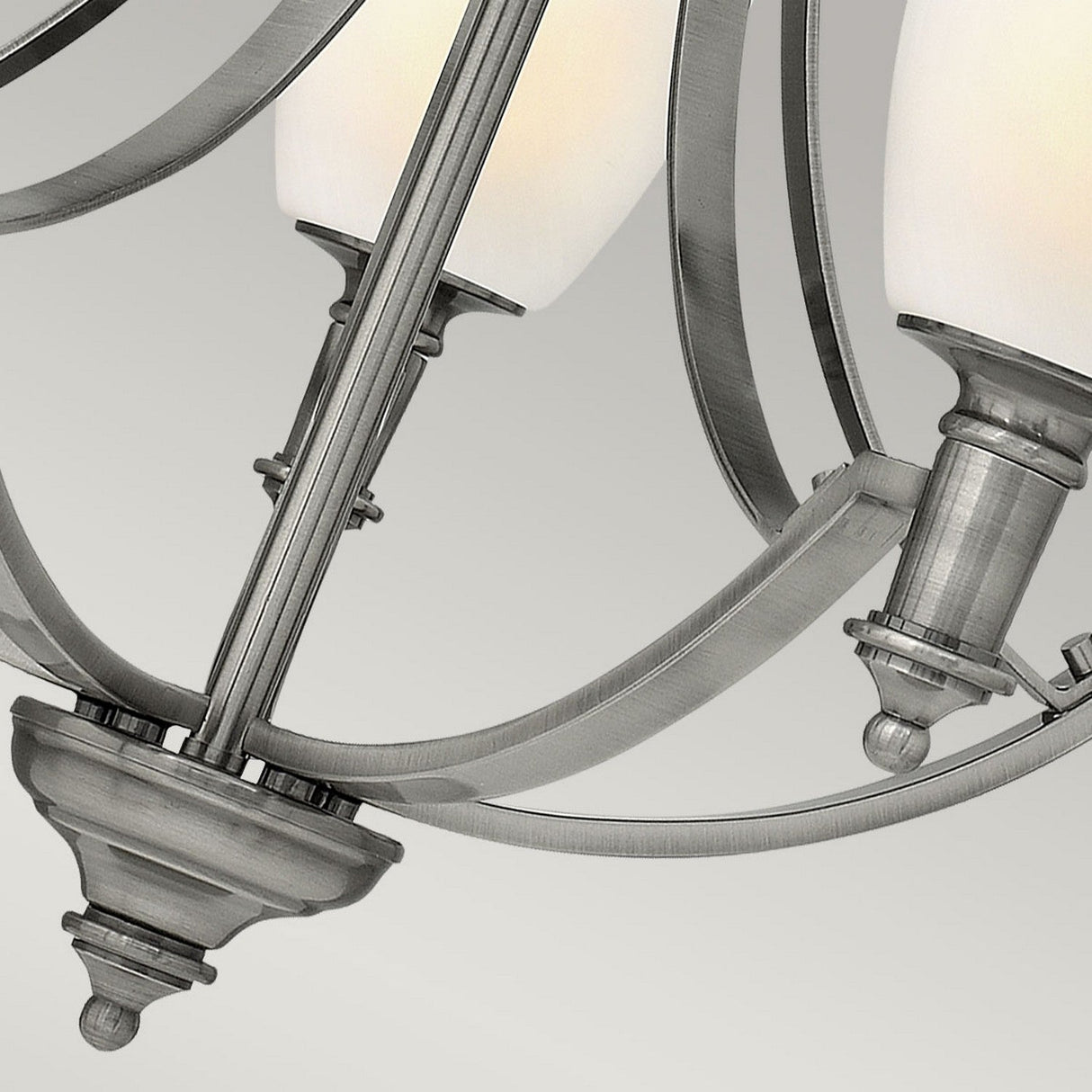 A detailed view of the Truman 5 Light Chandelier - Antique Nickel showcases its curved metal arms and frosted cylindrical glass shades against a light gray backdrop. This fixture features a modern design with a polished finish, highlighted by etched opal glass accents.