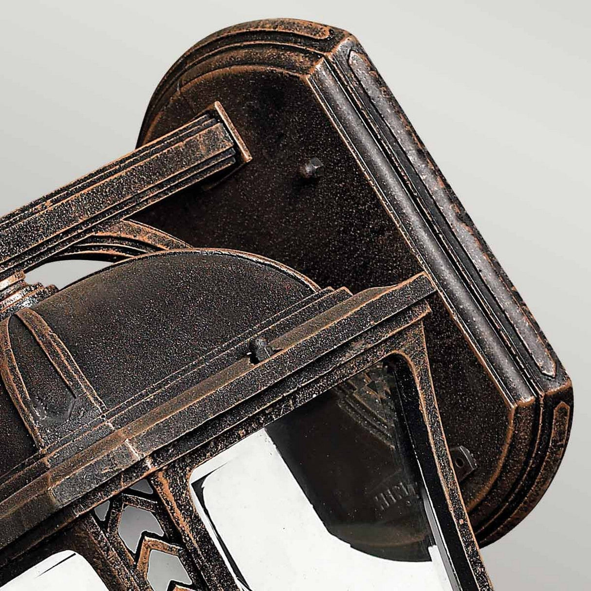 Close-up of the Wabash Outdoor 2 Light Medium Wall Lantern - Bronze mounted on the wall, showcasing its intricate metalwork and glass panes. The chevron design and rich patina finish lend this bronze wall lantern an antique look.