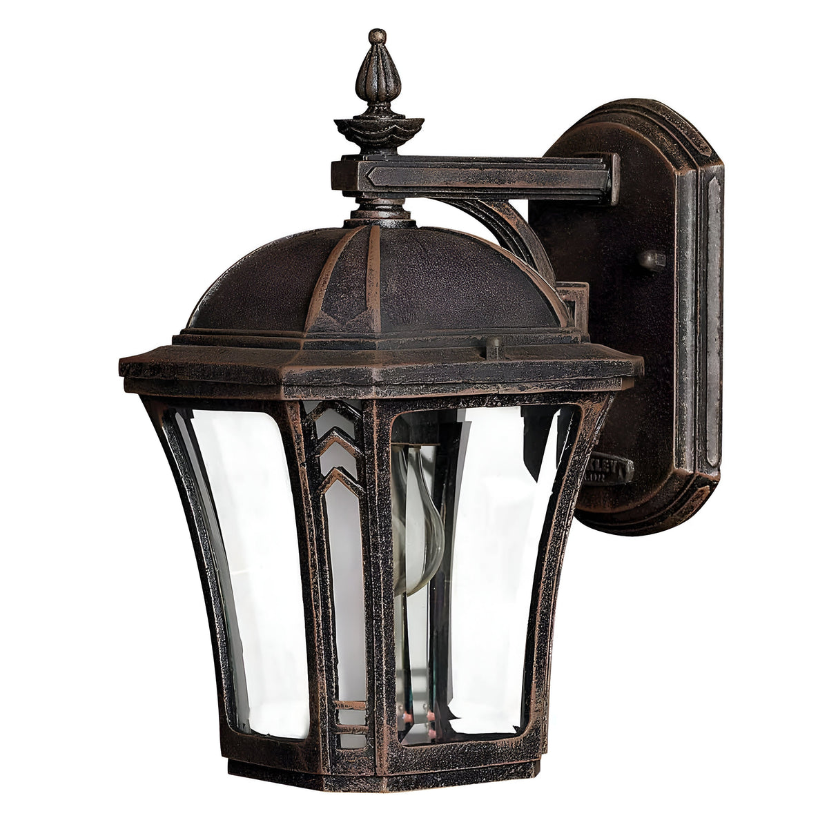 Introducing the Wabash Outdoor 1 Light Small Wall Lantern in Bronze: This vintage-style outdoor lighting piece features a decorative top and clear glass panels, complemented by a dark bronze finish. The mounted backplate is adorned with intricate detailing, while the chevron pattern enhances its elegant and classic appeal.