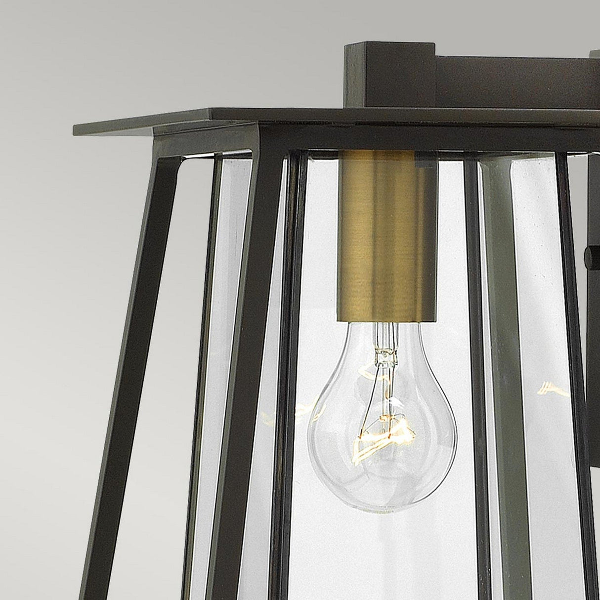 Close-up of the Walker Outdoor 1 Light Medium Wall Lantern, featuring a clear glass enclosure. Inside, a standard filament bulb is visible, secured by a fixture in Heritage Brass. The lantern's bronze frame blends contemporary design with rustic decor to enhance your outdoor lighting ambiance.