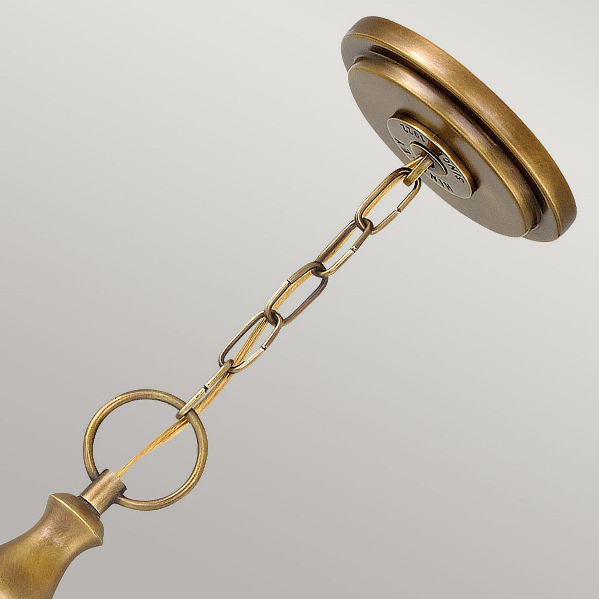 A close-up of the Wexley 3 Light Chandelier - Heritage Brass highlights its vintage brass chandelier chain and circular ceiling mount. The chain links elegantly connect the ceiling cap to the chandelier base, showcasing an antique finish in Heritage Brass against a neutral background, embodying transitional design elegance.