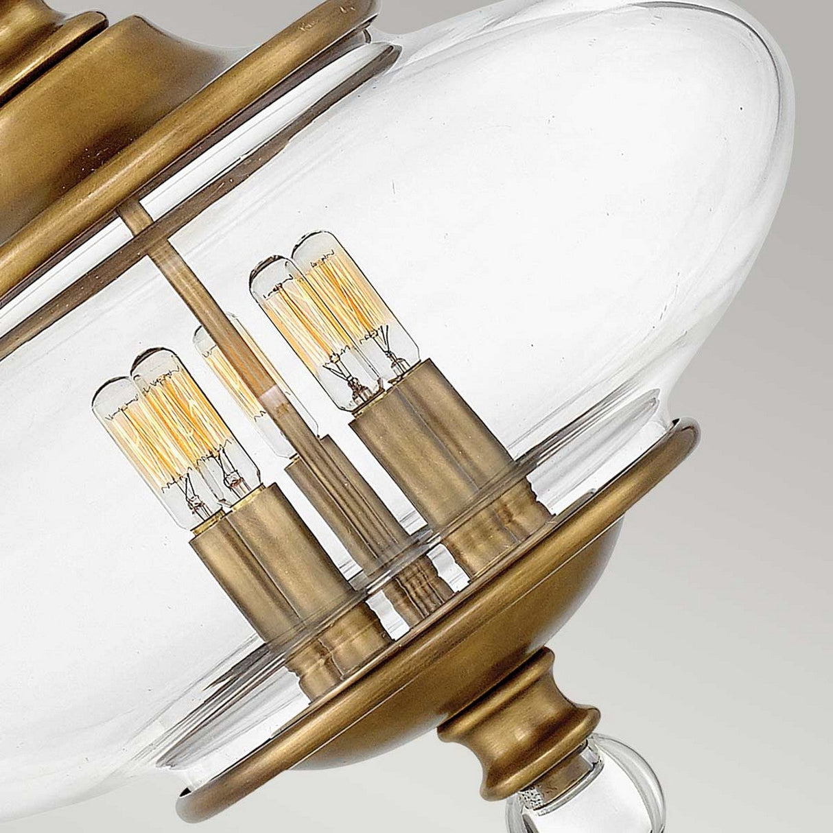 A close-up of the Wexley 5 Light Chandelier in Heritage Brass reveals its vintage-inspired charm, featuring a clear glass shade and exposed filament bulbs. The fixture is adorned with two vertical metal rods that support five bulbs, exuding elegance and a classic appearance.