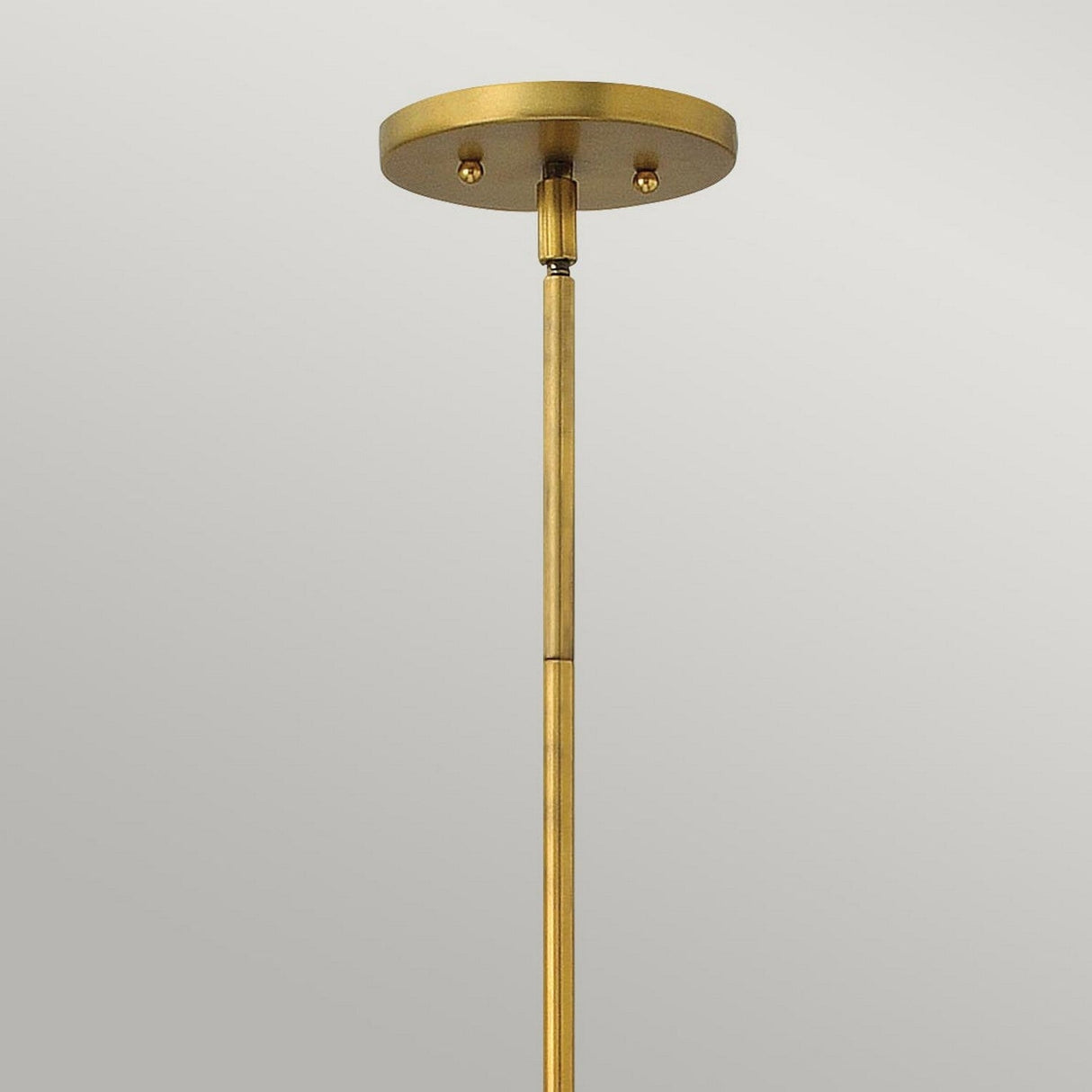 A close-up of the Zelda 1 Light Mini Pendant in Vintage Brass against a neutral background. The pendant features a rod extending down from a round, flat canopy, highlighting its simple and sleek mid-century design that adds timeless elegance to any space.