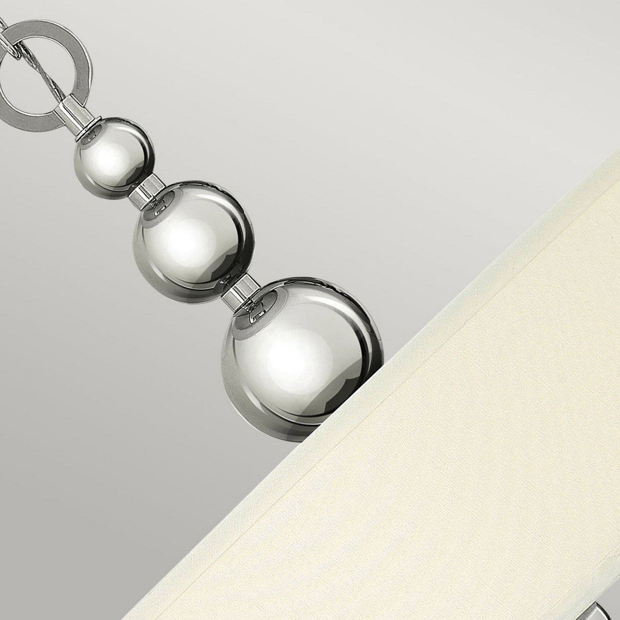 Close-up of the Zelda 3 Light Pendant - Polished Nickel with a beige shade, exuding mid-century charm. The vertical rod features three shiny spheres in polished nickel arranged in descending size, connected by thin rings. The background is a soft, neutral gray.