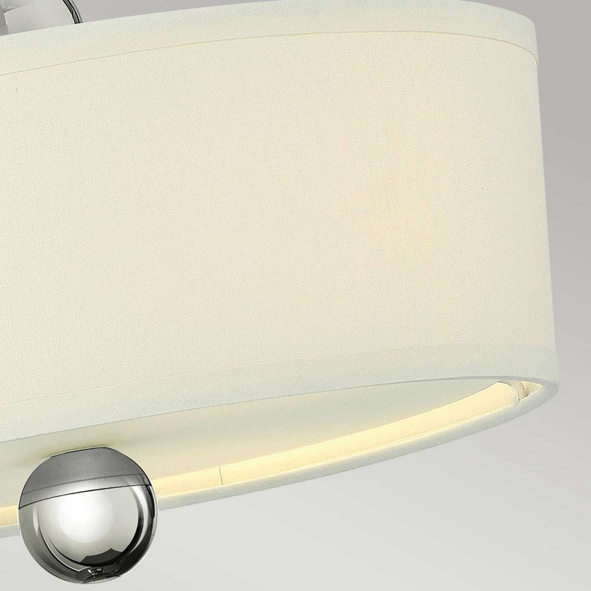 Close-up of the Zelda 3 Light Semi Flush ceiling light fixture showcasing a large cylindrical beige fabric lampshade. Below the shade, a small polished nickel detail hangs, providing a sleek and contemporary design contrast against a light gray background.