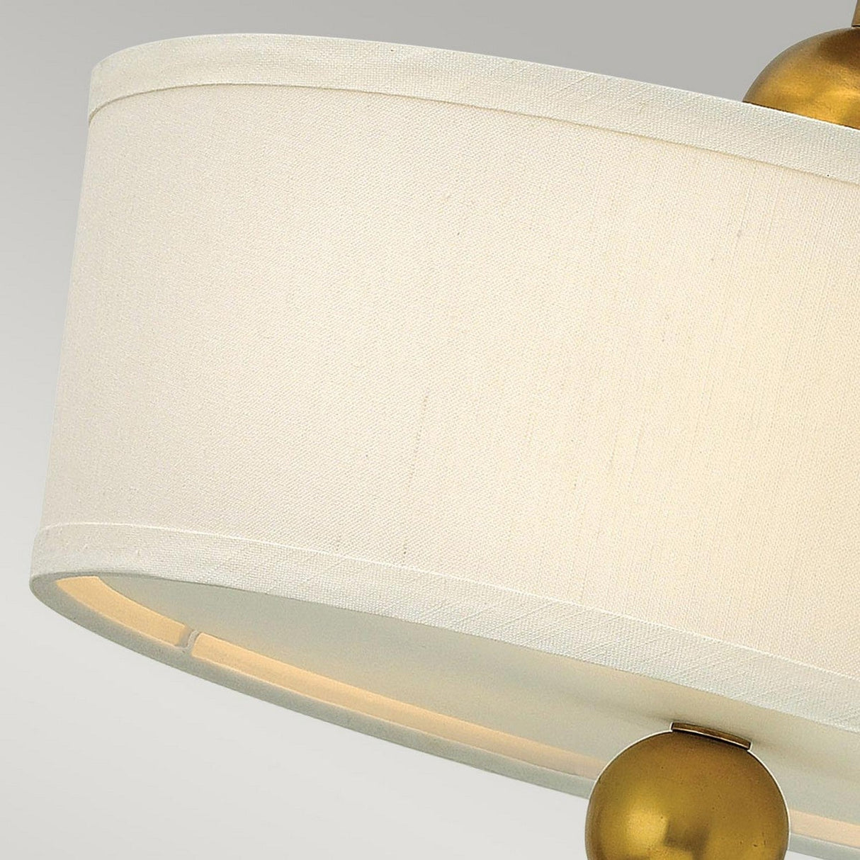 A close-up of the Zelda 3 Light Semi Flush features a beige fabric lampshade with a curved surface, accented by vintage brass spherical details. The image highlights the upper portion of this mid-century design fixture against a neutral gray background.