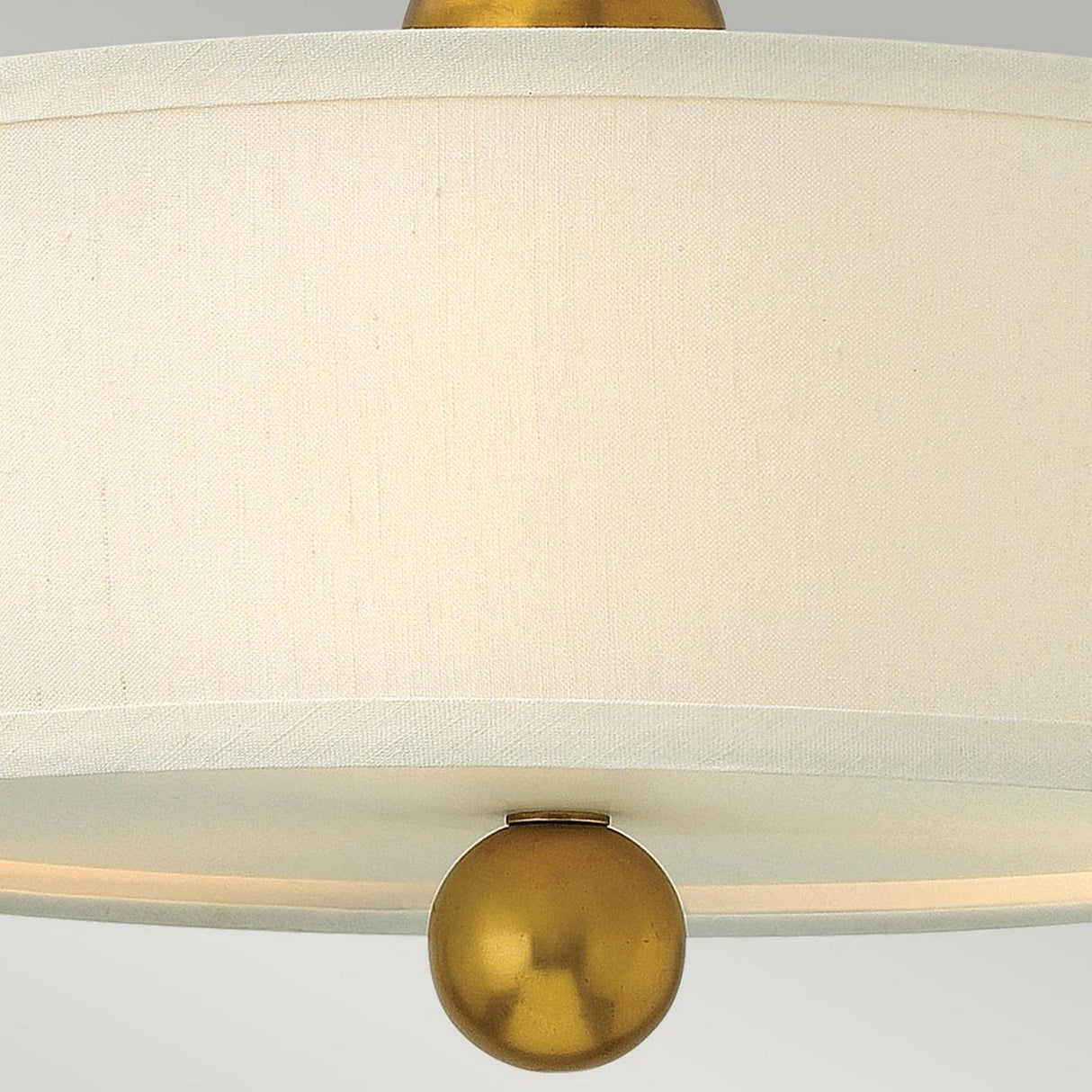 Close-up of the Zelda 3 Light Semi Flush in Vintage Brass, showcasing a beige fabric shade and a central vintage brass sphere accent at the bottom, set against a plain, light gray background.
