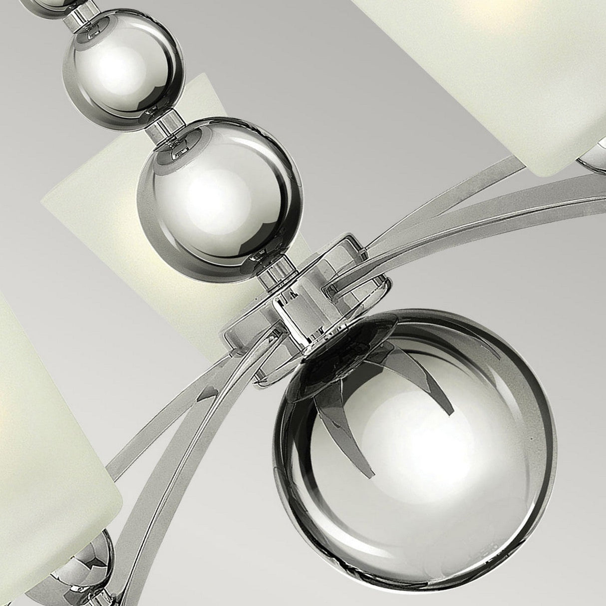 Close-up of the Zelda 5 Light Chandelier - Polished Nickel, featuring a polished nickel frame adorned with spherical glass accents. This fixture captures mid-century sophistication with its frosted glass shades, presenting a sleek and contemporary design against a light gray background.