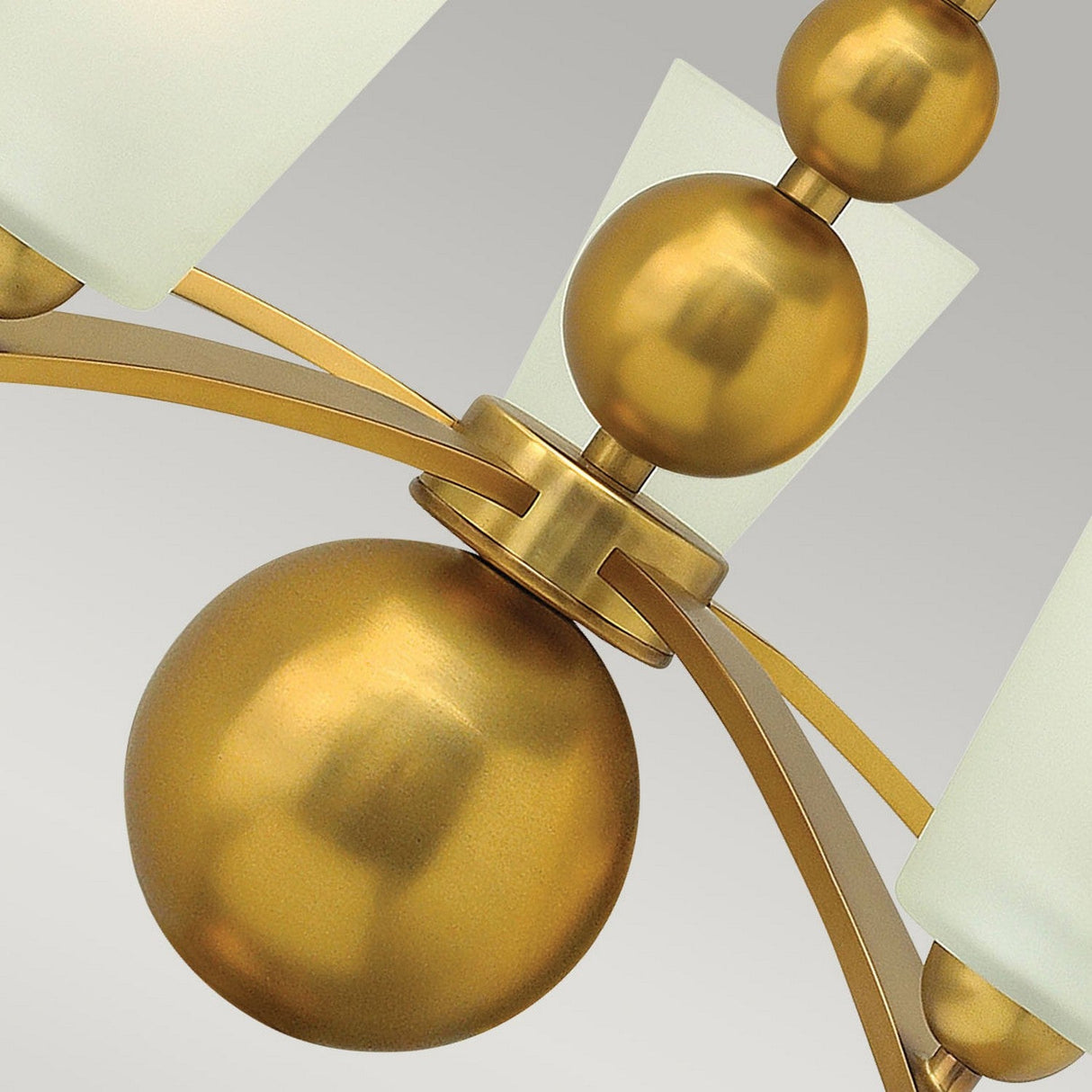 Close-up of the Zelda 5 Light Chandelier - Vintage Brass, showcasing its mid-century design with spherical gold accents and frosted glass shades, elegantly arranged on metal arms against a light gray background.