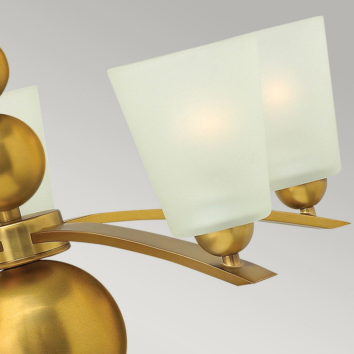 Detailed view of the Zelda 5 Light Chandelier in vintage brass, showcasing its frosted square lampshades adorned with an etched glass shade detail. Two of the lampshades are prominently displayed, beautifully mounted on gracefully curved metal arms. The design artfully merges mid-century style with contemporary sophistication set against a plain background.