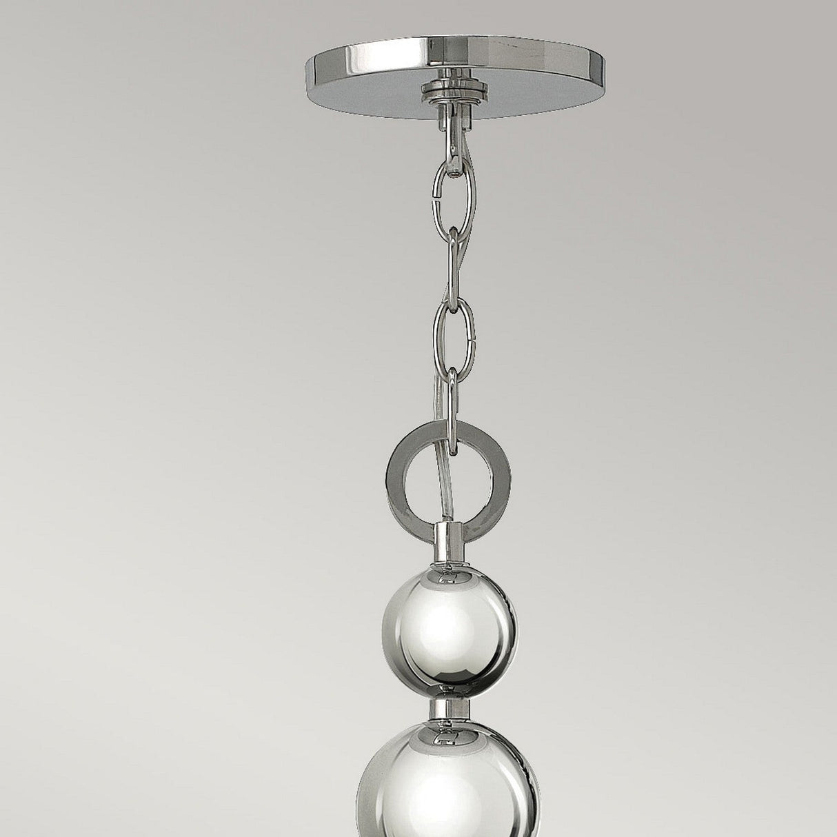 Close-up of the Zelda 8 Light Chandelier in polished nickel, featuring a sleek silver metal chain and two polished nickel spheres. The chandelier, inspired by mid-century design, is suspended from a round ceiling plate against a light gray background.