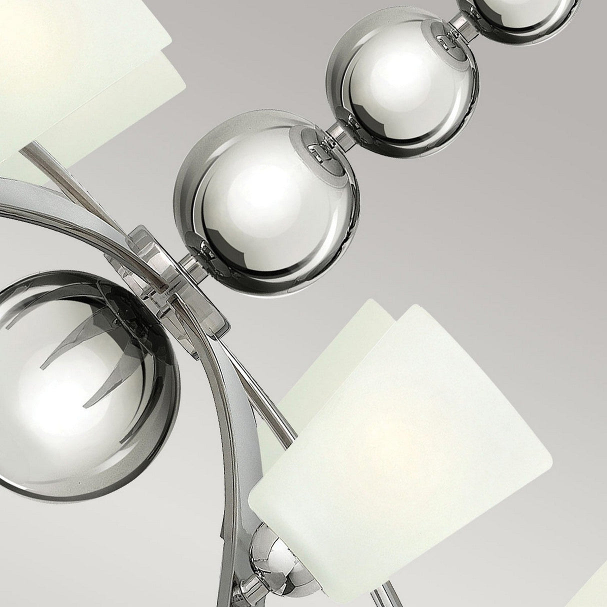 Close-up of the Zelda 8 Light Chandelier - Polished Nickel, showcasing its polished nickel spheres and frosted square glass shades on a sleek metal frame, exuding a mid-century design allure against a gray background.