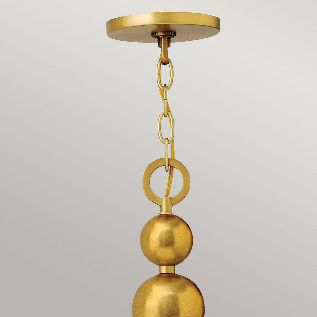 A close-up of a modern gold pendant light fixture with a linked chain and spherical design evokes mid-century aesthetics. This fixture, akin to the Zelda 8 Light Chandelier in Vintage Brass, is suspended from a circular ceiling mount against a neutral backdrop.